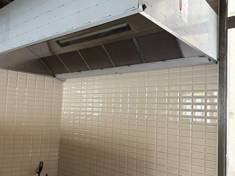Hotte professionnelle inox neuve à filtres installée dans un local carrelé en cours d'aménagement