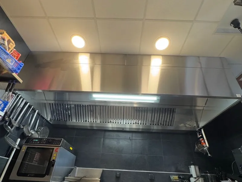 Hotte murale inox à filtres à chocs avec éclairage au-dessus d'un plan de cuisson